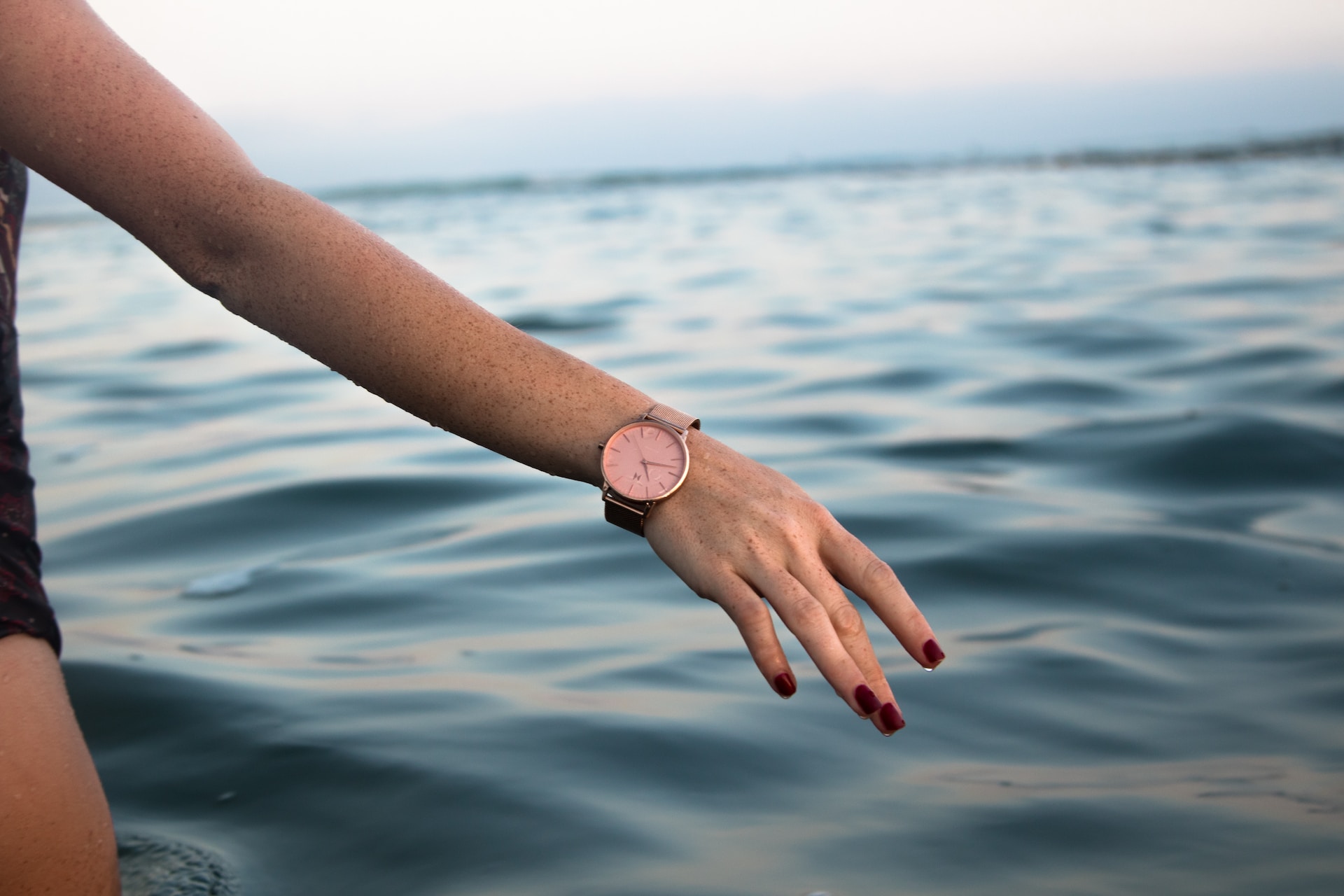 A close-up of a woman’s arm over gentle water, emphasizing her wrist watch.