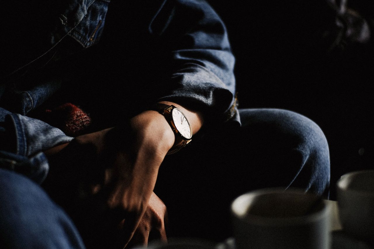 A man leans forward in a coffee shop, wearing a watch.