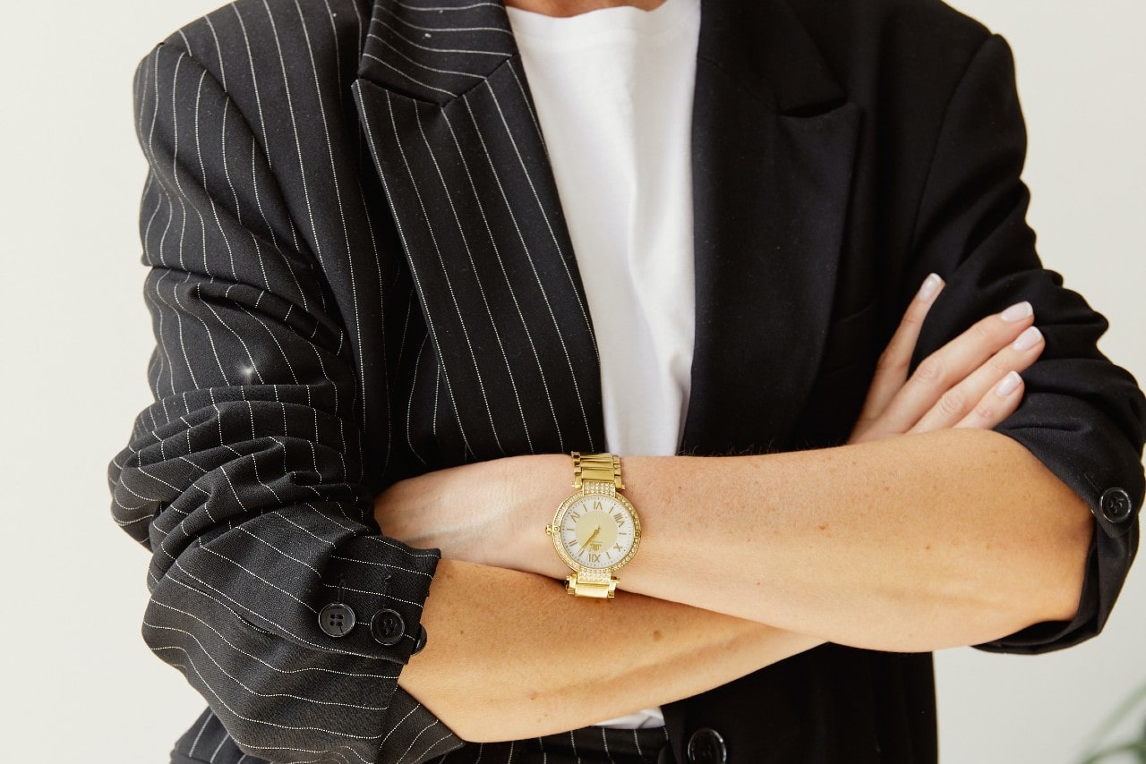 A close-up of a well-dressed person with folded arms, emphasizing their dress watch.