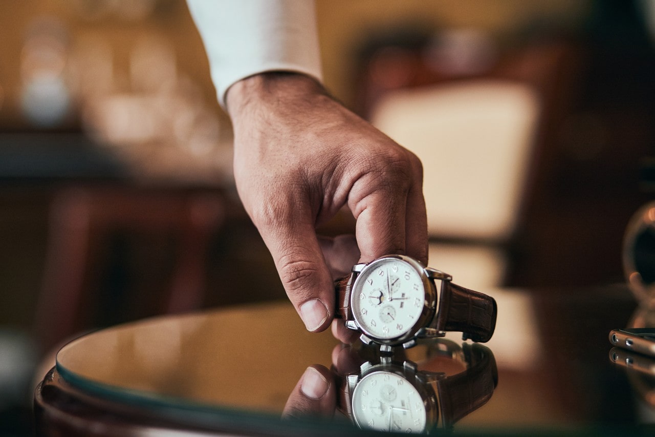 A close-up of a man’s hand picking up a luxury watch from an elegant table.