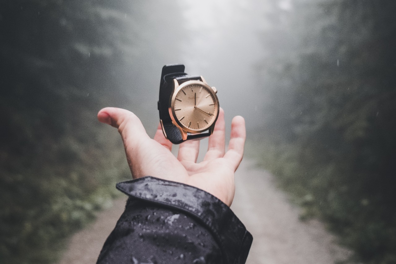 A person’s hand holding an elegant watch in their hand, outside in the rain.