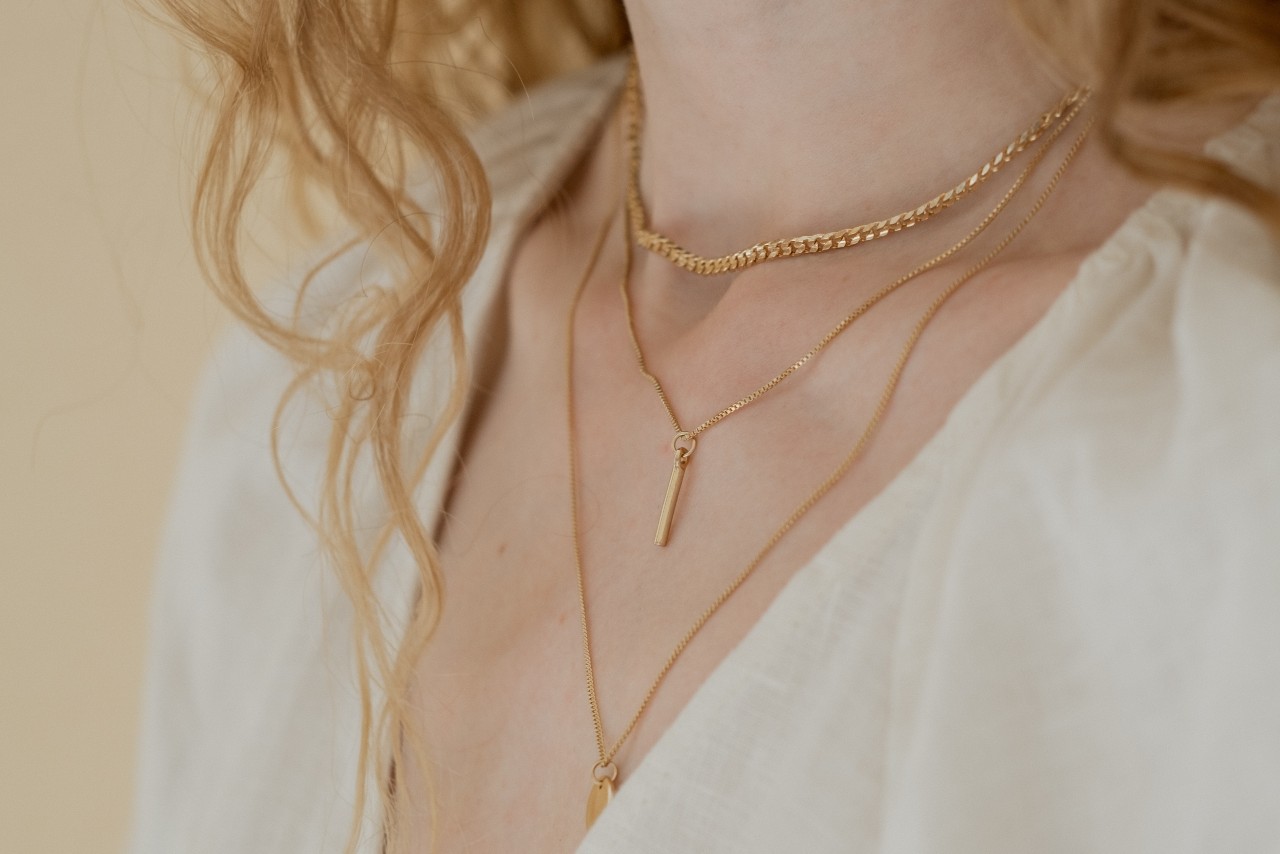 close up image of a woman’s neckline wearing three layered gold necklaces