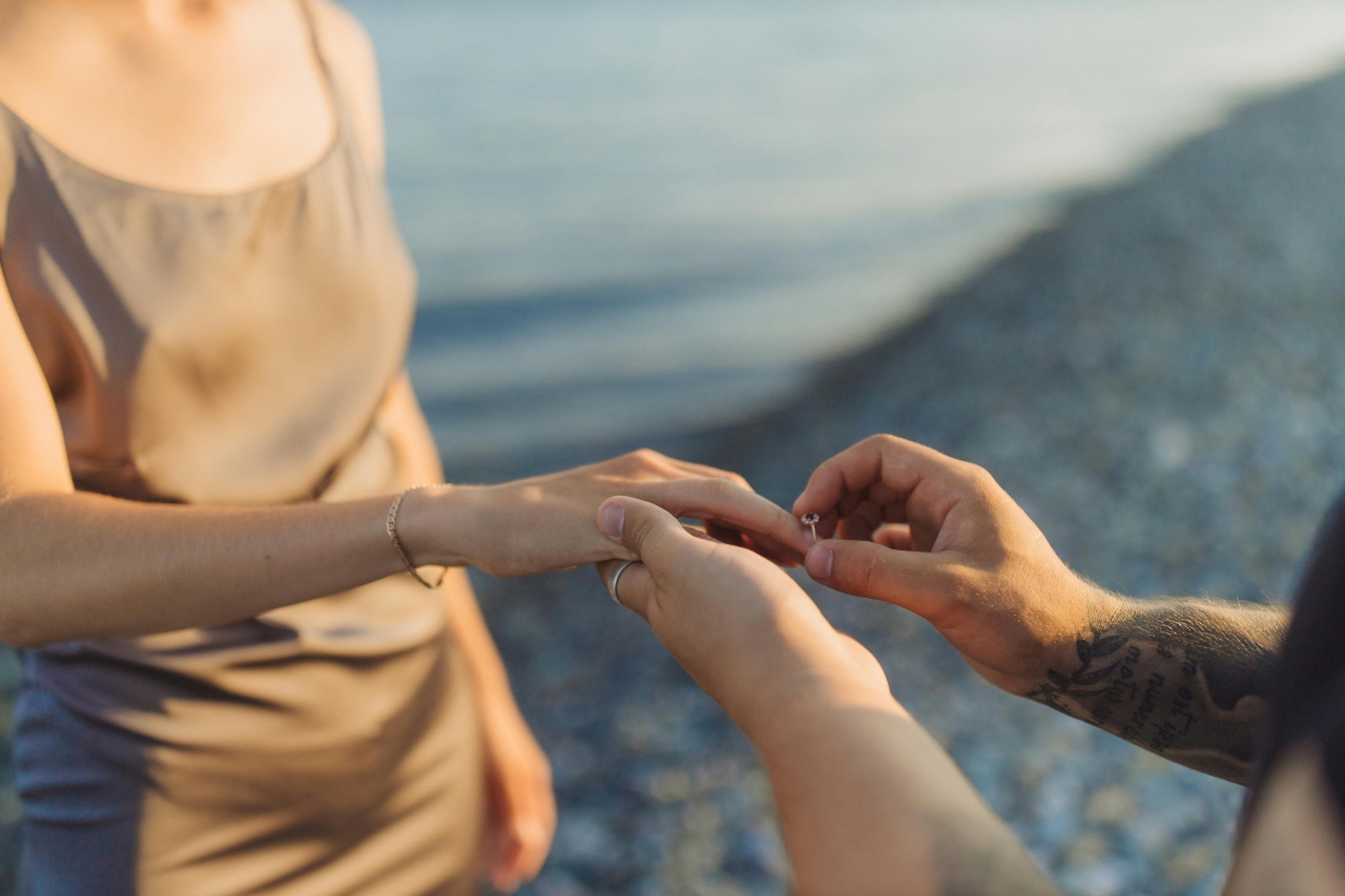 a man slipping an engagement ring on a woman’s finger on the beach