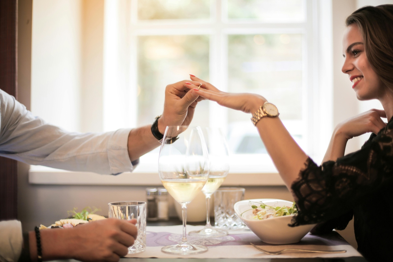 a man proposing to a woman at a dinner table and slipping a ring on her finger