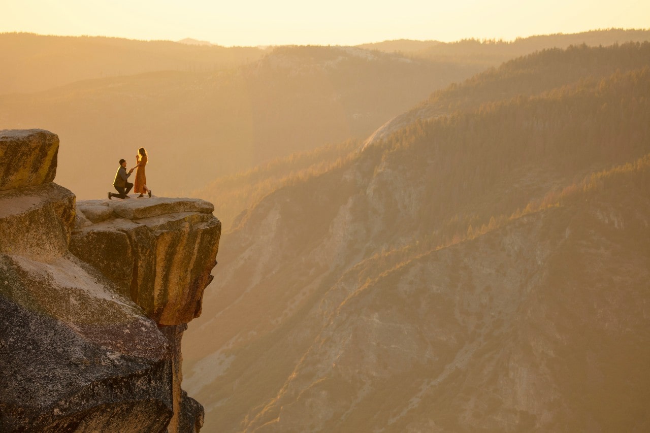 a man proposing to a woman on a cliff’s edge near a huge valley