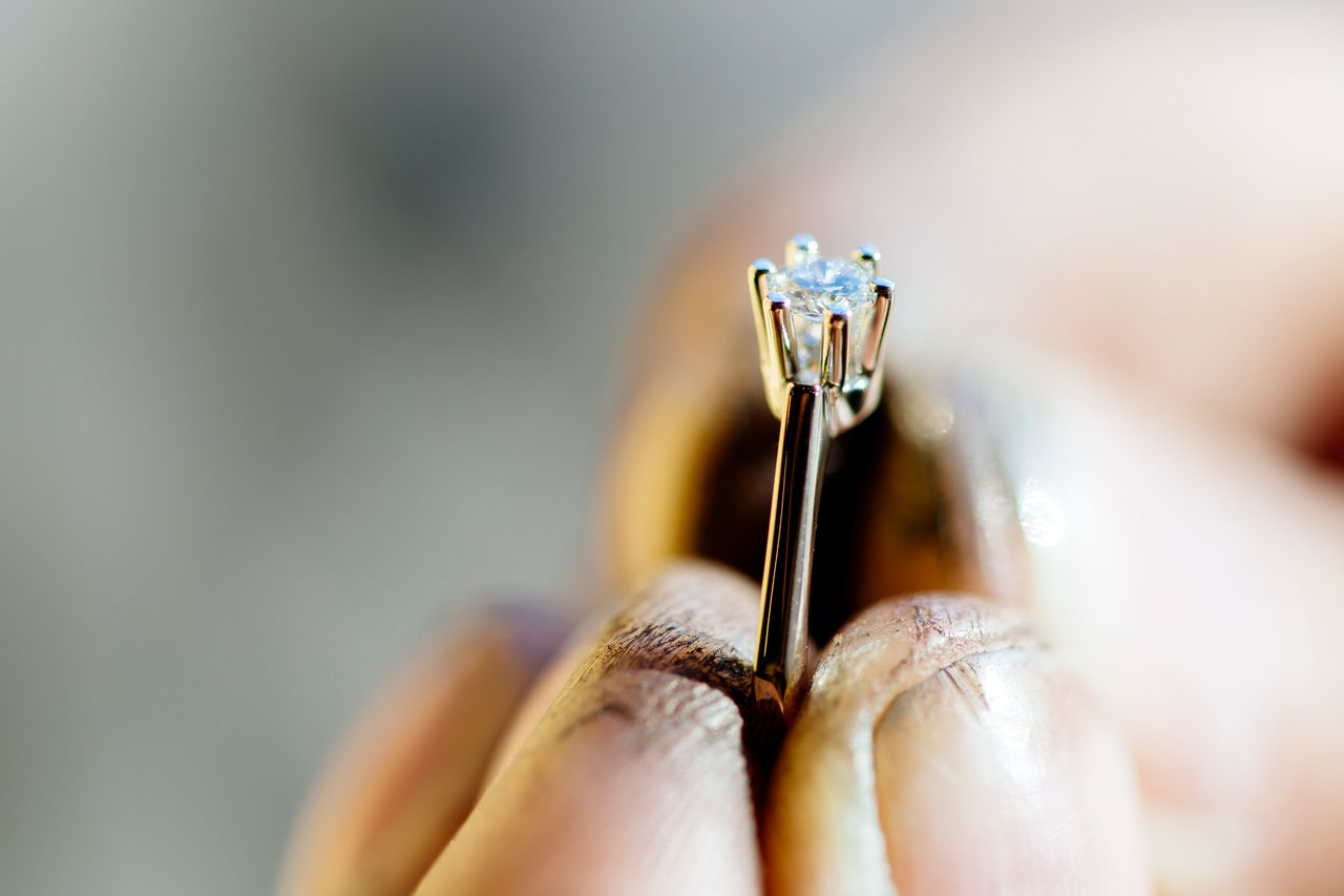 A close-up of a man’s hands holding a delicate engagement ring by its sizing bar.