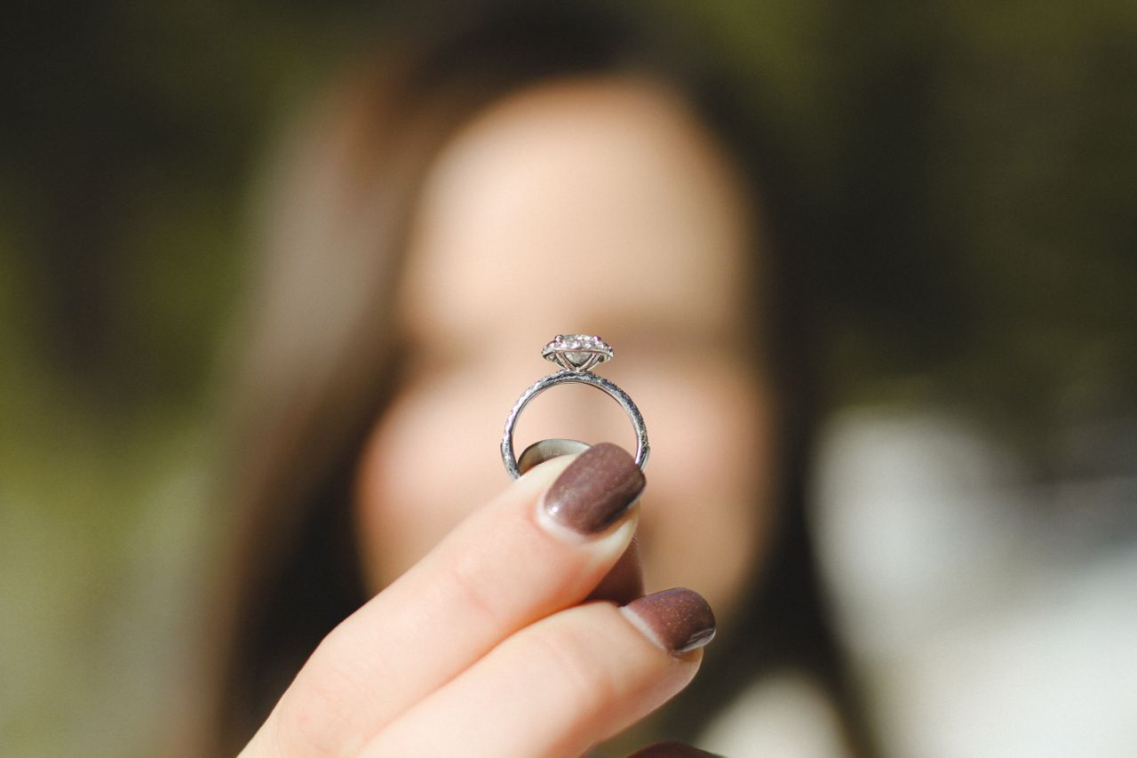 A close-up of a woman’s manicured hand holding a white gold engagement ring.