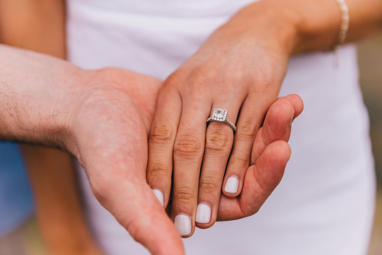 A close-up of a couple hand-in-hand, emphasizing the bride-to-be’s engagement ring.