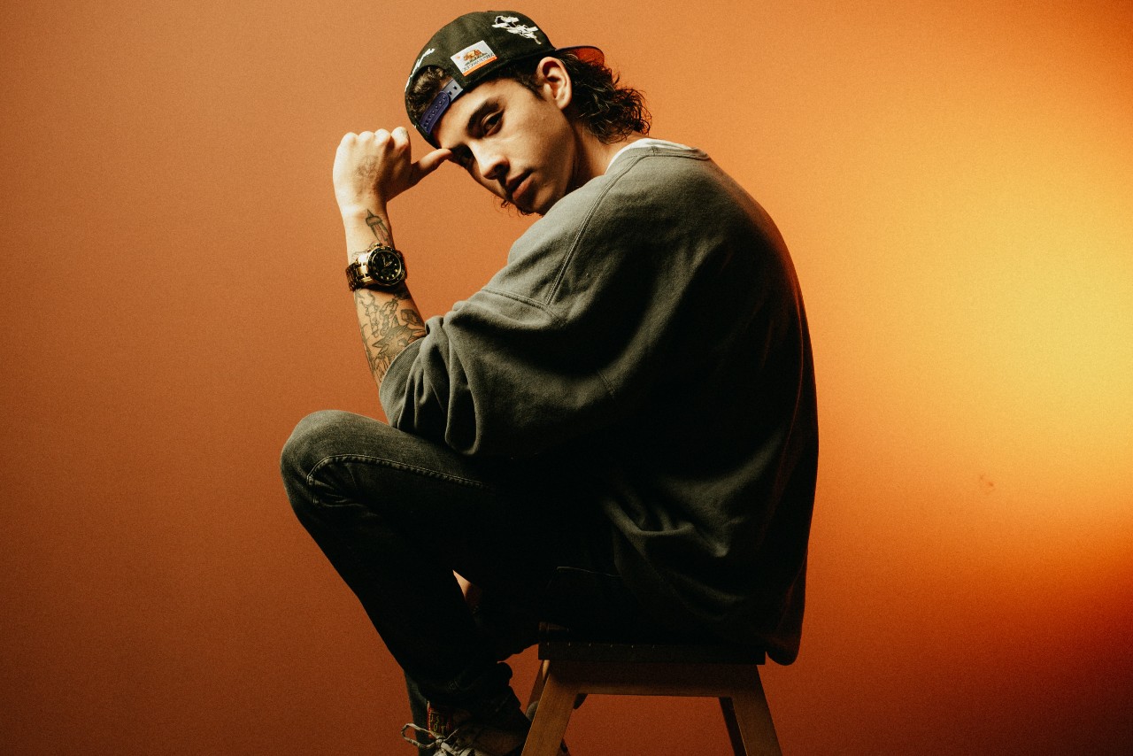 a young man sitting on a stool and wearing a ball cap and a black watch