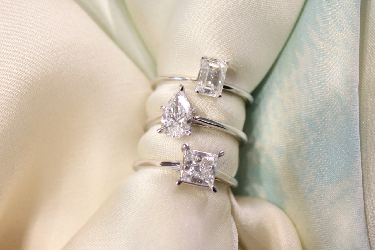 A close-up of three white gold solitaire diamond engagement rings stacked on a cloth napkin.