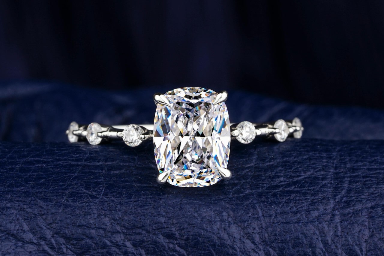 A close-up image of a diamond engagement ring with side stones on a leather surface.