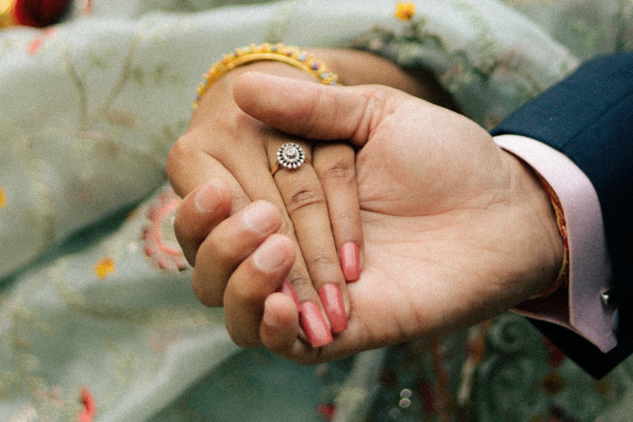 a man holding a woman’s hand who is wearing a halo engagement ring