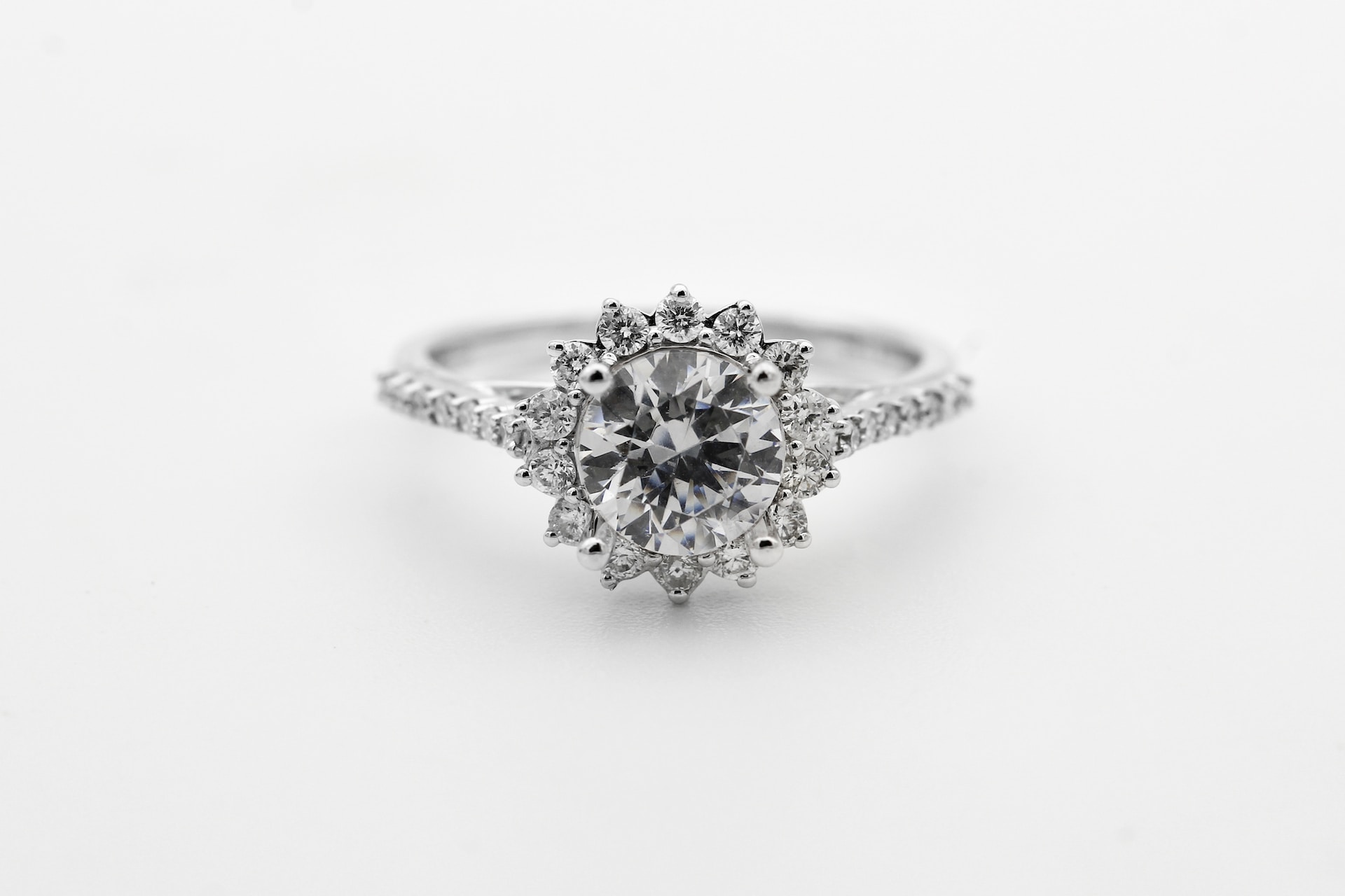 a round cut engagement ring featuring a halo of diamonds and side stones