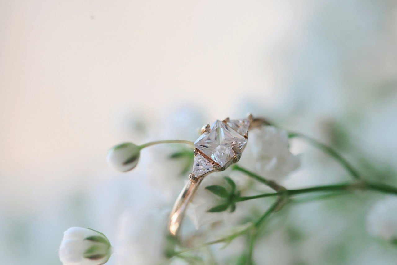 A gold, three stone engagement ring, on a spring of white flowers