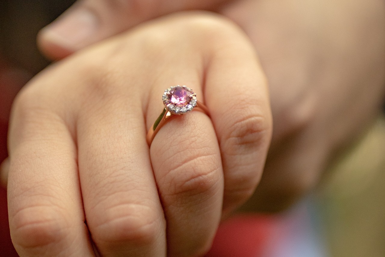 A rose gold halo engagement ring with a purple center stone on a woman’s hand.