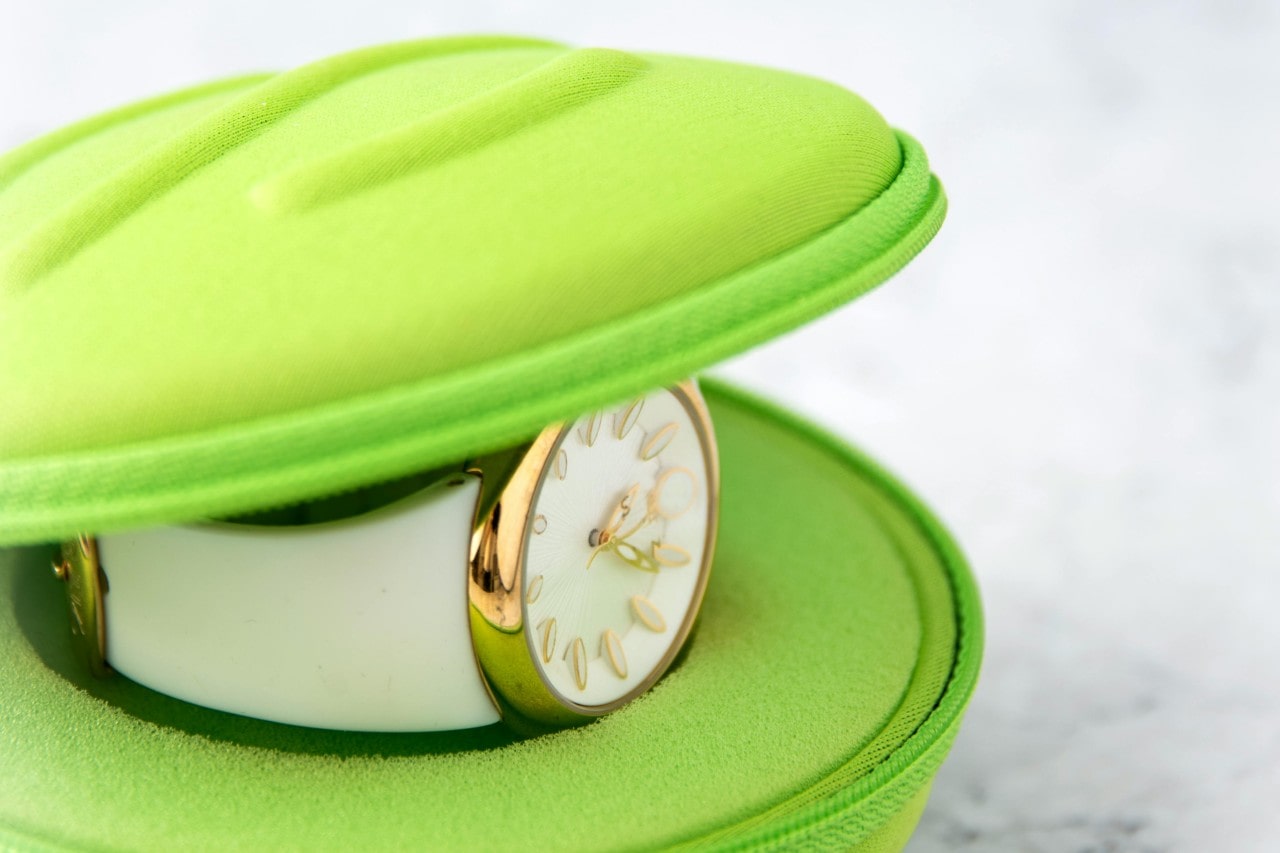 A close-up of a stunning and minimalist gold watch displayed in a chartreuse clamshell.