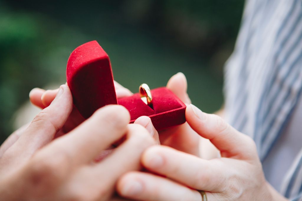 Proposal with a gold wedding band in the red velvet box