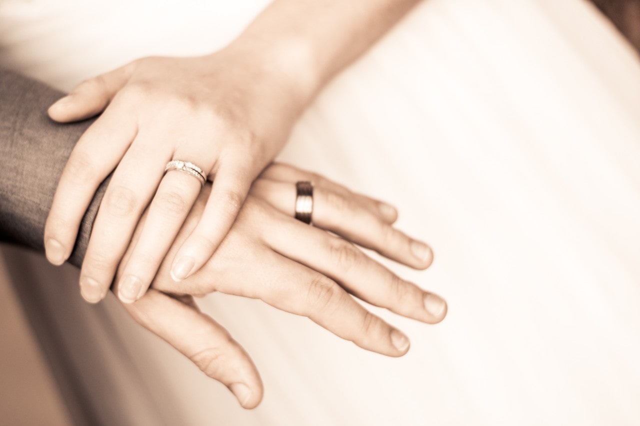 Bride’s hand resting and groom’s hand with gold wedding bands