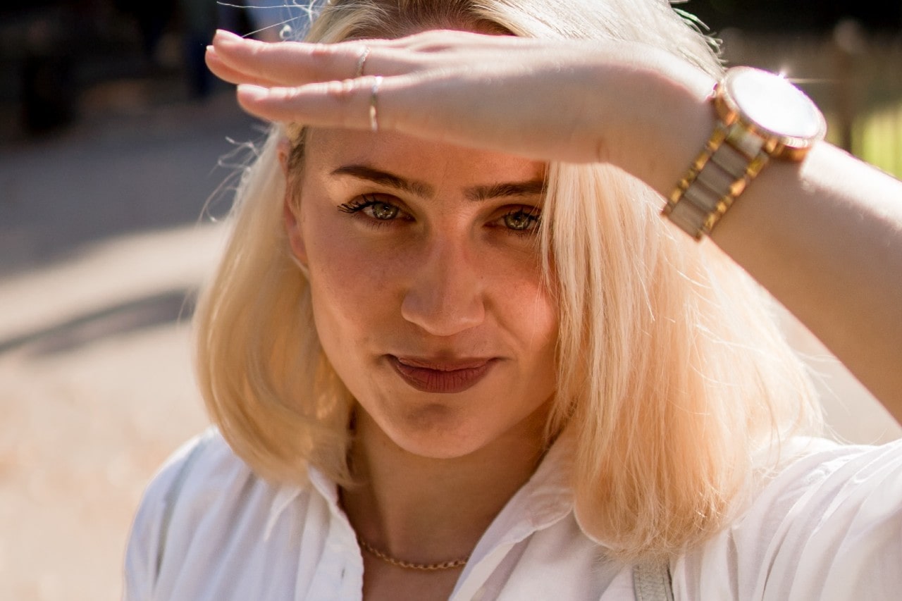 a woman shading her eyes from the sun and wearing a mixed metal watch