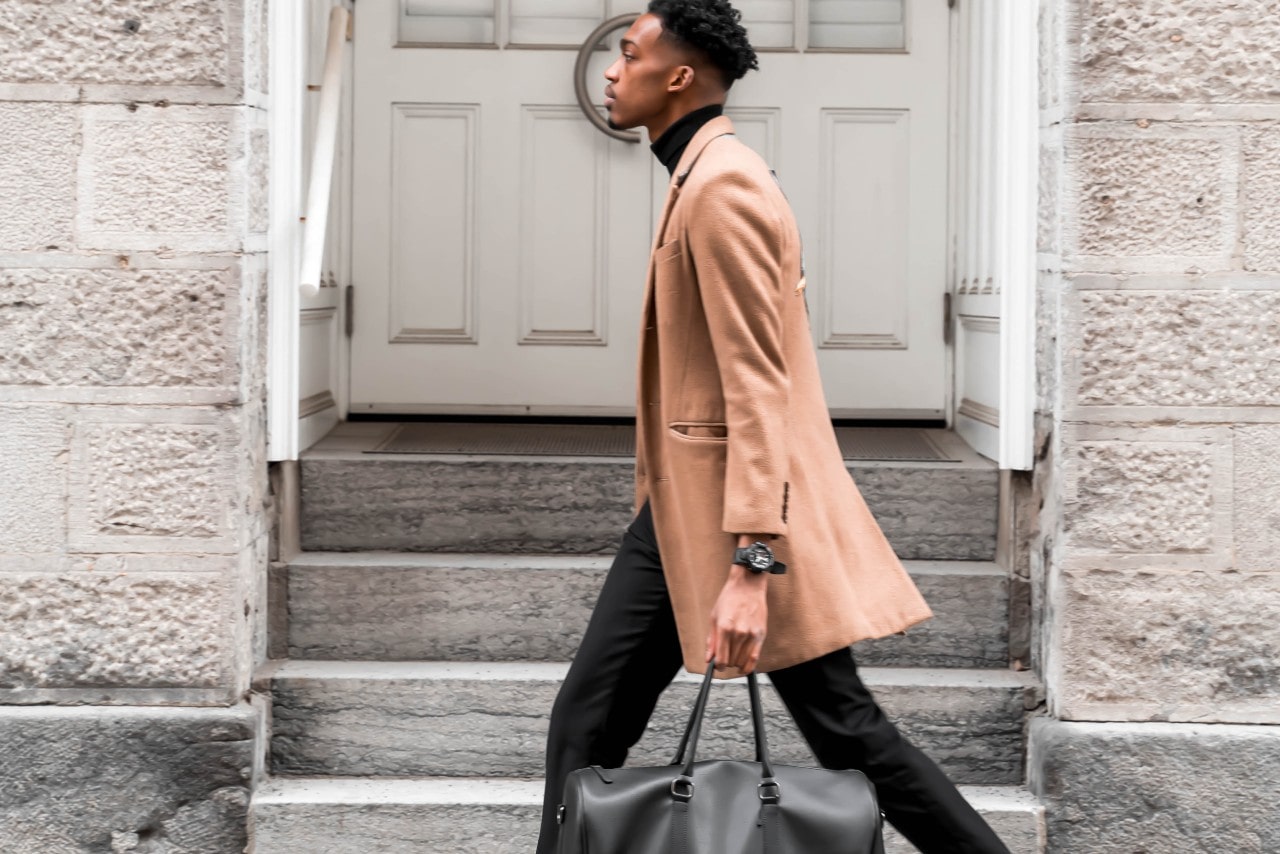 a man walking down the street wearing a brown coat and a black watch