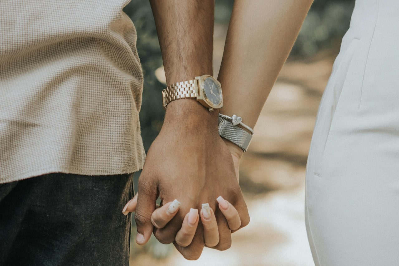 A close-up of a couple holding hands, both wearing wrist watches.