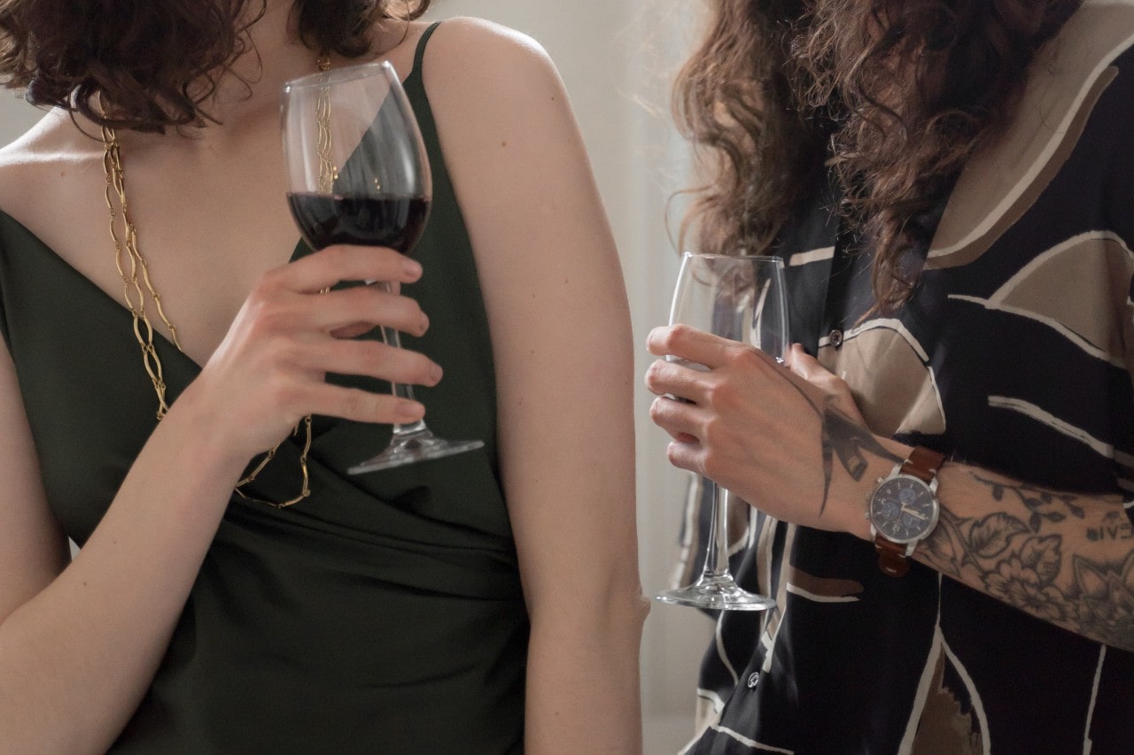 two formal women drinking red wine at a party.