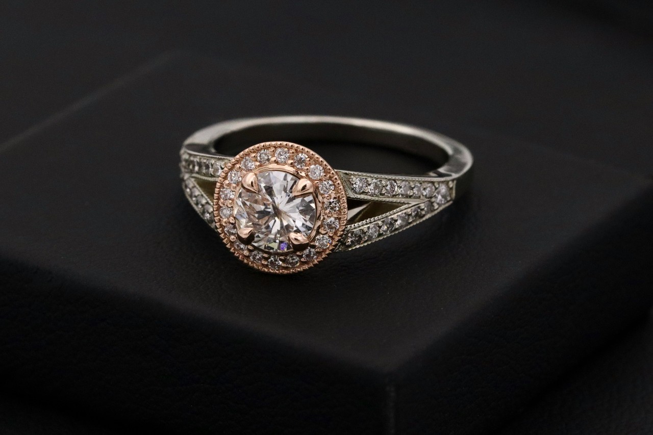 A mixed metal engagement ring featuring a halo, sidestones, and milgrain details.