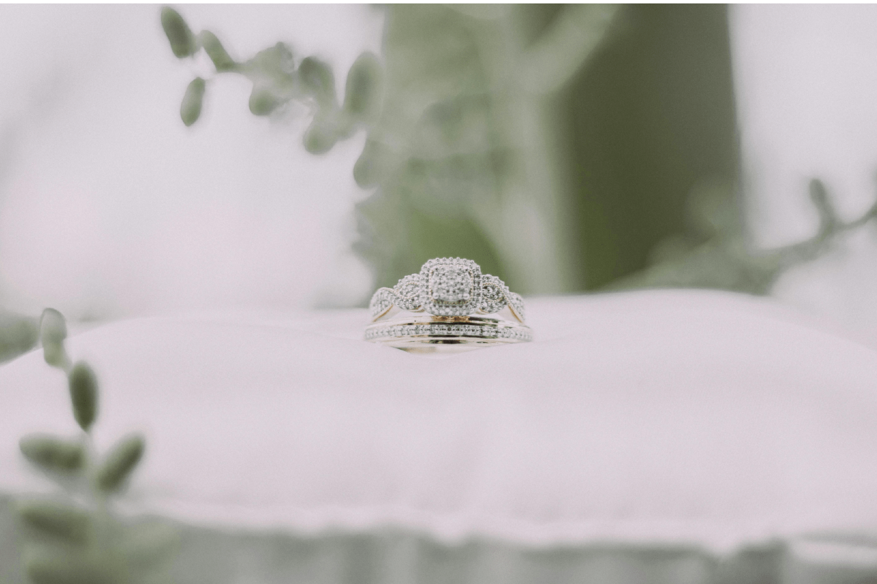 A matching set of bridal rings on a white pillow surrounded by greenery.