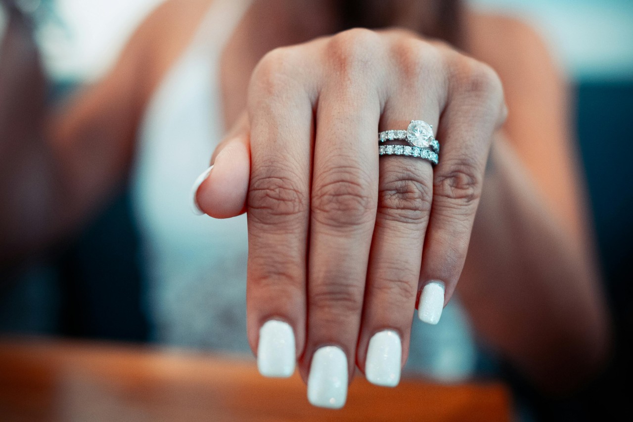 A close-up of a bride-to-be’s hand, adorned with an elegant side-stone engagement ring and matching band.