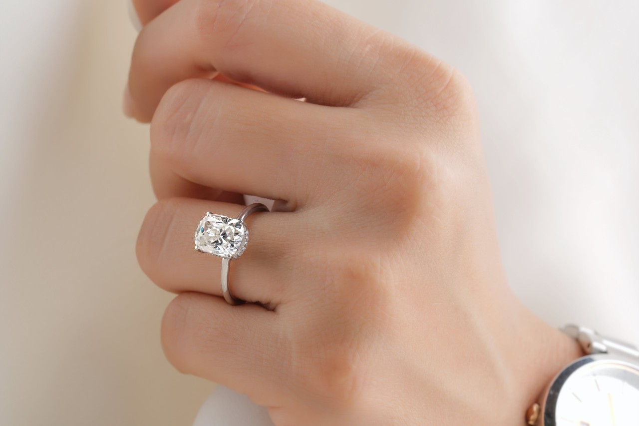 A close-up of a woman’s hand, wearing an elegant solitaire engagement ring.