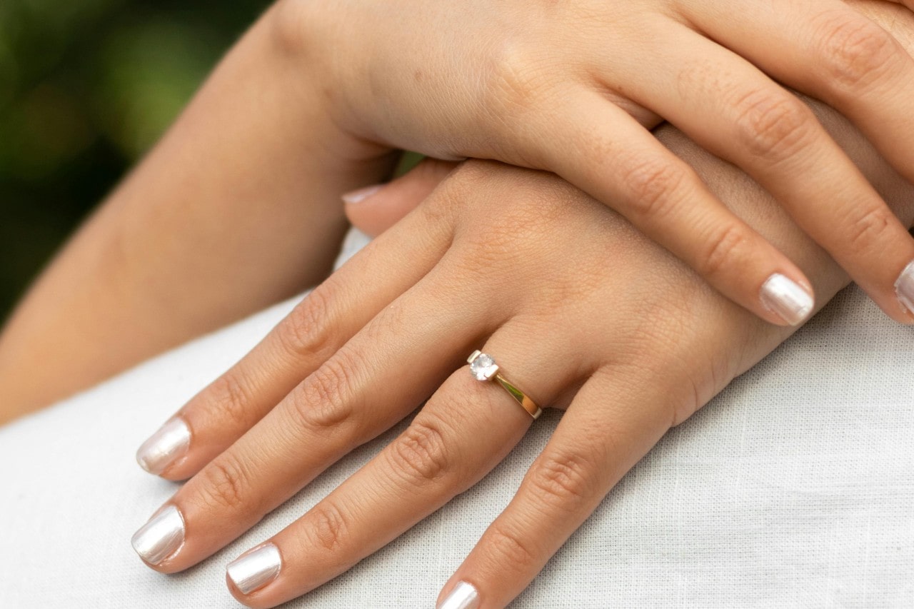 A close-up of a bride-to-be’s hands, adorned in a solitaire engagement ring as she embraces her groom.