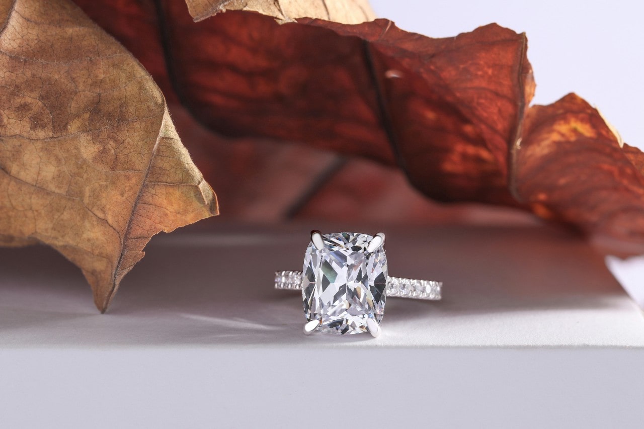 A close-up of a side-stone engagement ring displayed in front of autumn leaves.