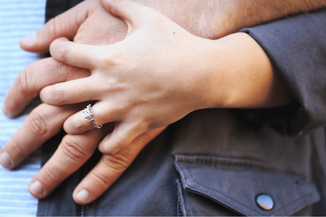 A close-up of a woman’s hand holding that of her partner, her hand adorned with a two tone engagement ring.