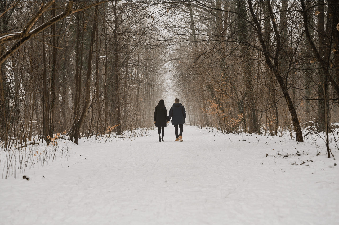 A faraway shot of a couple holding hands as they walk down a snowy path on a cold winter day.